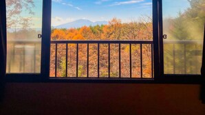 A room with a large window overlooking a balcony with autumn foliage and distant mountains.