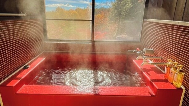 A hot tub with a view of autumn trees and a clear sky through a large window.