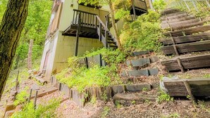 A traditional building with a staircase leading up to a balcony, surrounded by lush greenery.