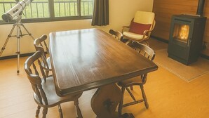A spacious room with a large wooden dining table, a telescope, and a wood-burning stove.