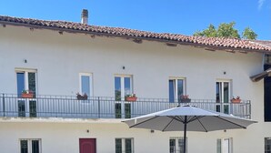 A courtyard with a wooden table and chairs, surrounded by potted plants and a red door. - Marvelous farmhouse with AC in Rocchetta Tanaro - 5 bedrooms (Rocchetta Tanaro)