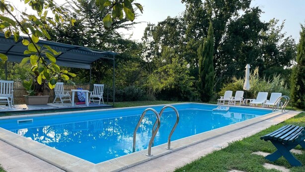 A rectangular swimming pool with a tiled edge, surrounded by a grassy area and a covered seating area with white chairs. - Marvelous farmhouse with AC in Rocchetta Tanaro - 5 bedrooms (Rocchetta Tanaro)