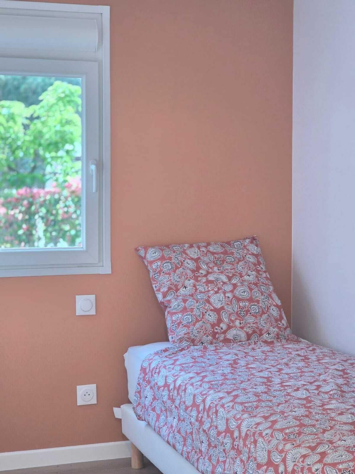 Une chambre avec un lit simple, une fenêtre et une prise de courant au mur.