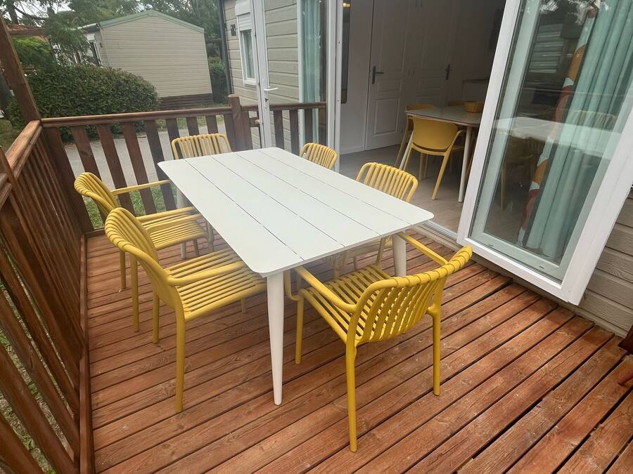 A covered patio with a white table and yellow chairs, wooden deck, and a sliding glass door leading to a garage.