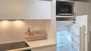 Una cocina compacta con armarios blancos, un microondas, horno integrado y un refrigerador.