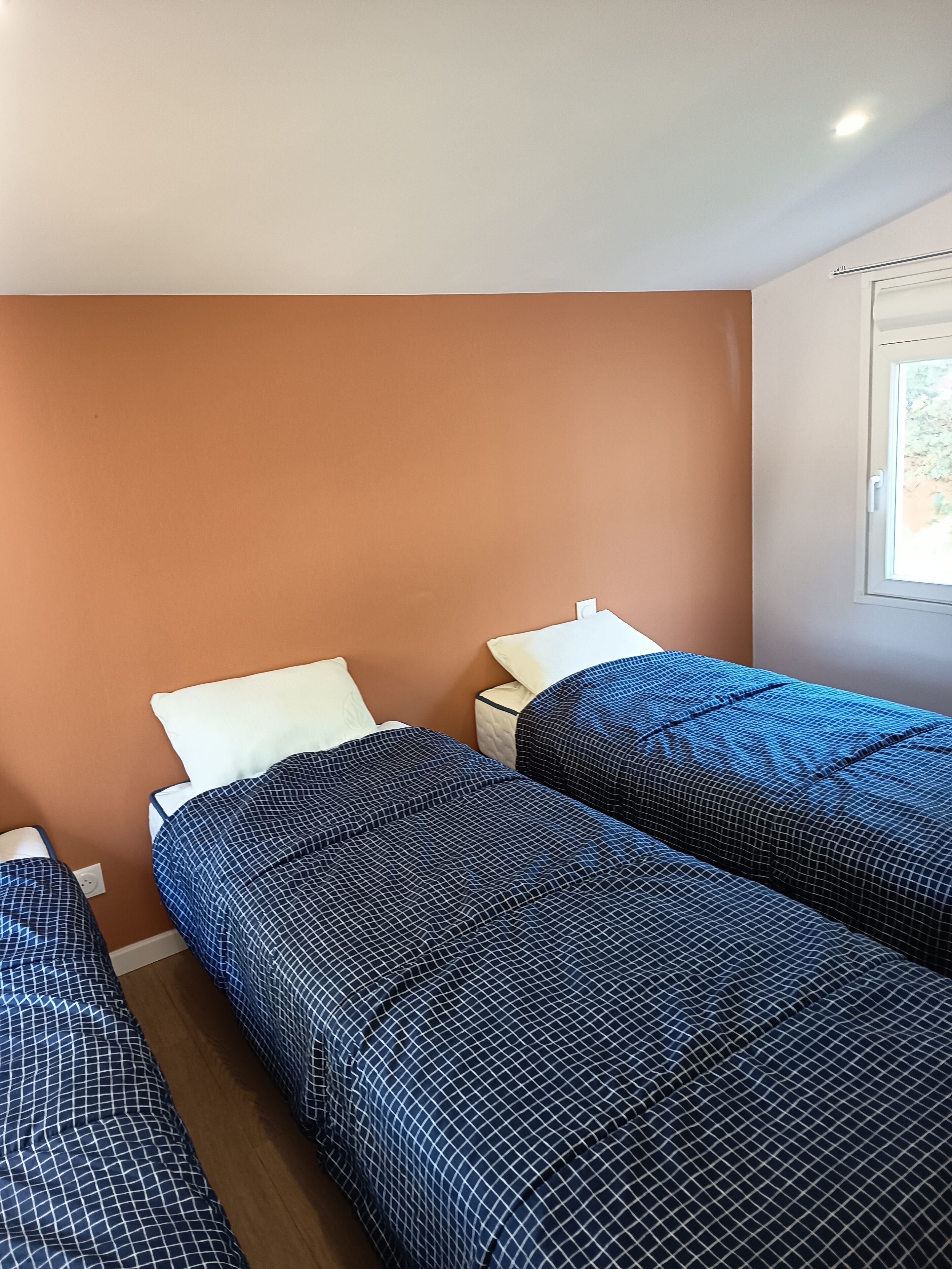 Una habitación con dos camas, cada una con una colcha azul y blanca estampada, un almohón blanco y una mesita de noche con una lámpara.