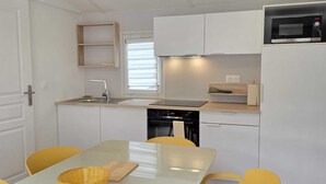 Una cocina moderna con armarios blancos, un microondas Bosch y una lámpara colgante amarilla.
