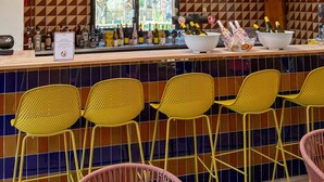 Una zona de bar con luces colgantes de malla roja, sillas amarillas y un revoque de azulejos.