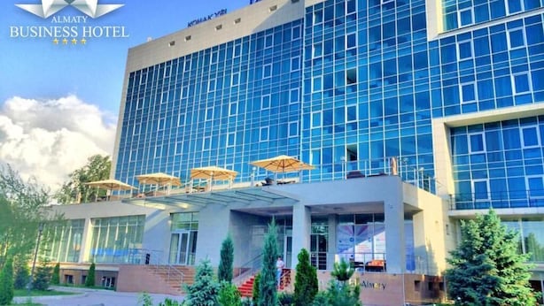 Un hotel moderno para negocios con fachada de vidrio, asientos al aire libre y una entrada ajardinada.