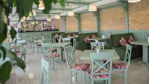 Un restaurante con paredes verdes, varias mesas y sillas, y lámparas colgantes.