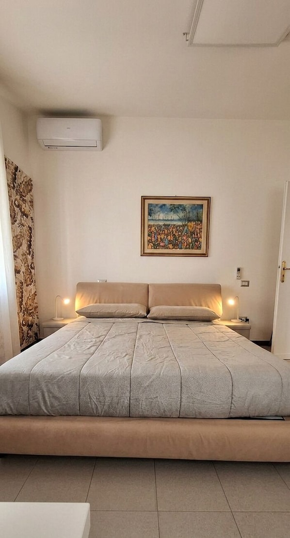 Une chambre à coucher avec un lit, un tableau au mur, un appareil de climatisation et une table de chevet avec une lampe.