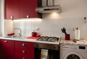 Une cuisine équipée d’une cuisinière à gaz, d’un lave-linge et de meubles de rangement rouges.