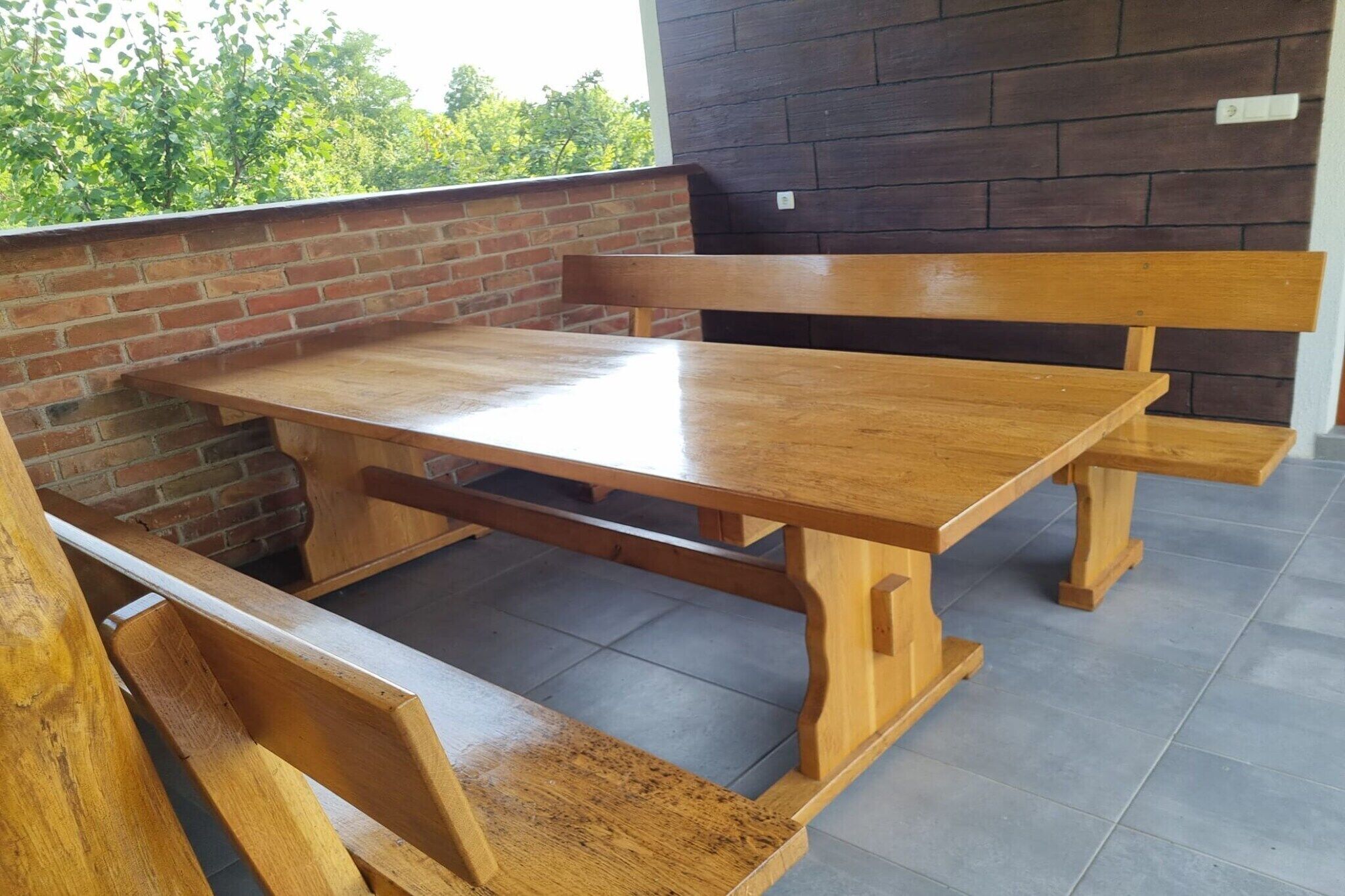 Mesa y bancos de madera en un balcón con pared de ladrillo y suelo de baldosas.