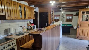 Une cuisine avec des meubles en bois, un four encastré, un four à micro-ondes et, au fond, une table de billard.
