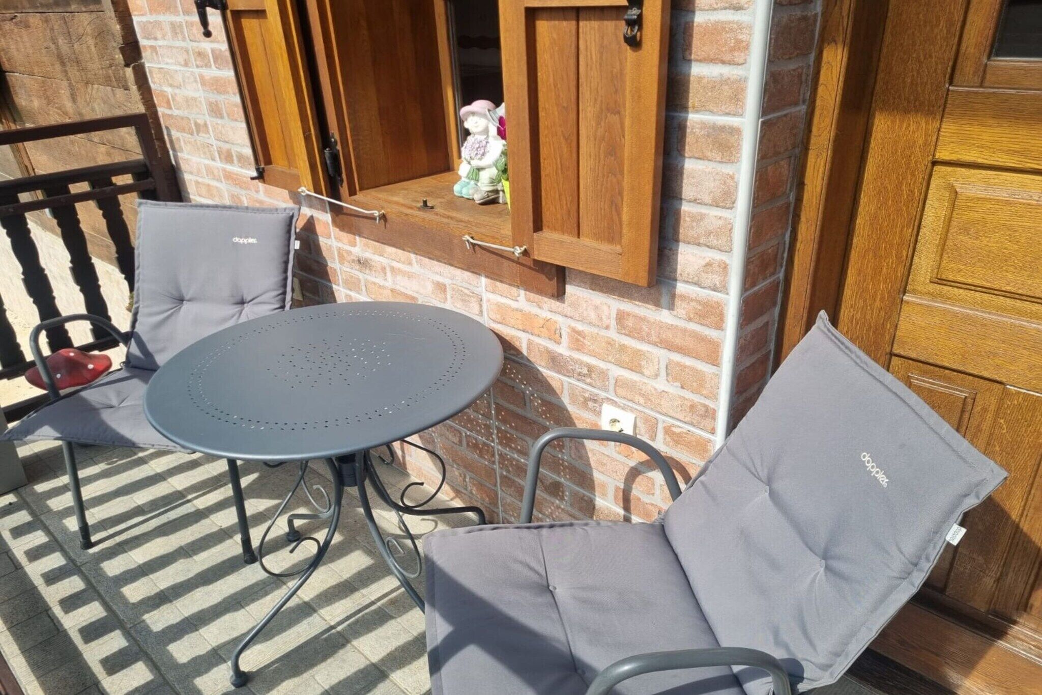 A patio with a round table and two chairs, a wooden cabinet with a window, and a brick wall.