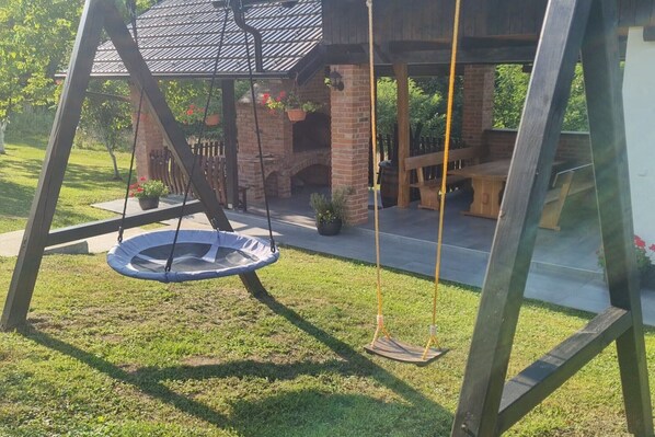 A swing set with a hanging seat and a brick patio area with outdoor seating.