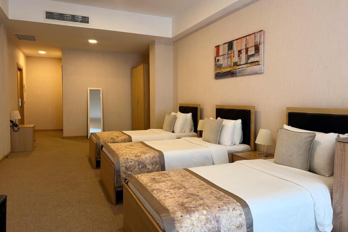 A hotel room with four beds, a large mirror, a painting on the wall, and a carpeted floor.