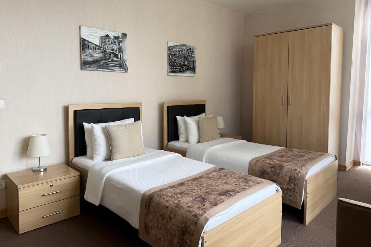 A hotel room with two beds, a wardrobe, a nightstand, and two wall-mounted paintings.