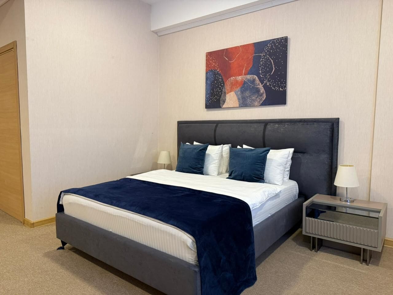Un dormitorio con cama, mesitas de noche y un cuadro en la pared.