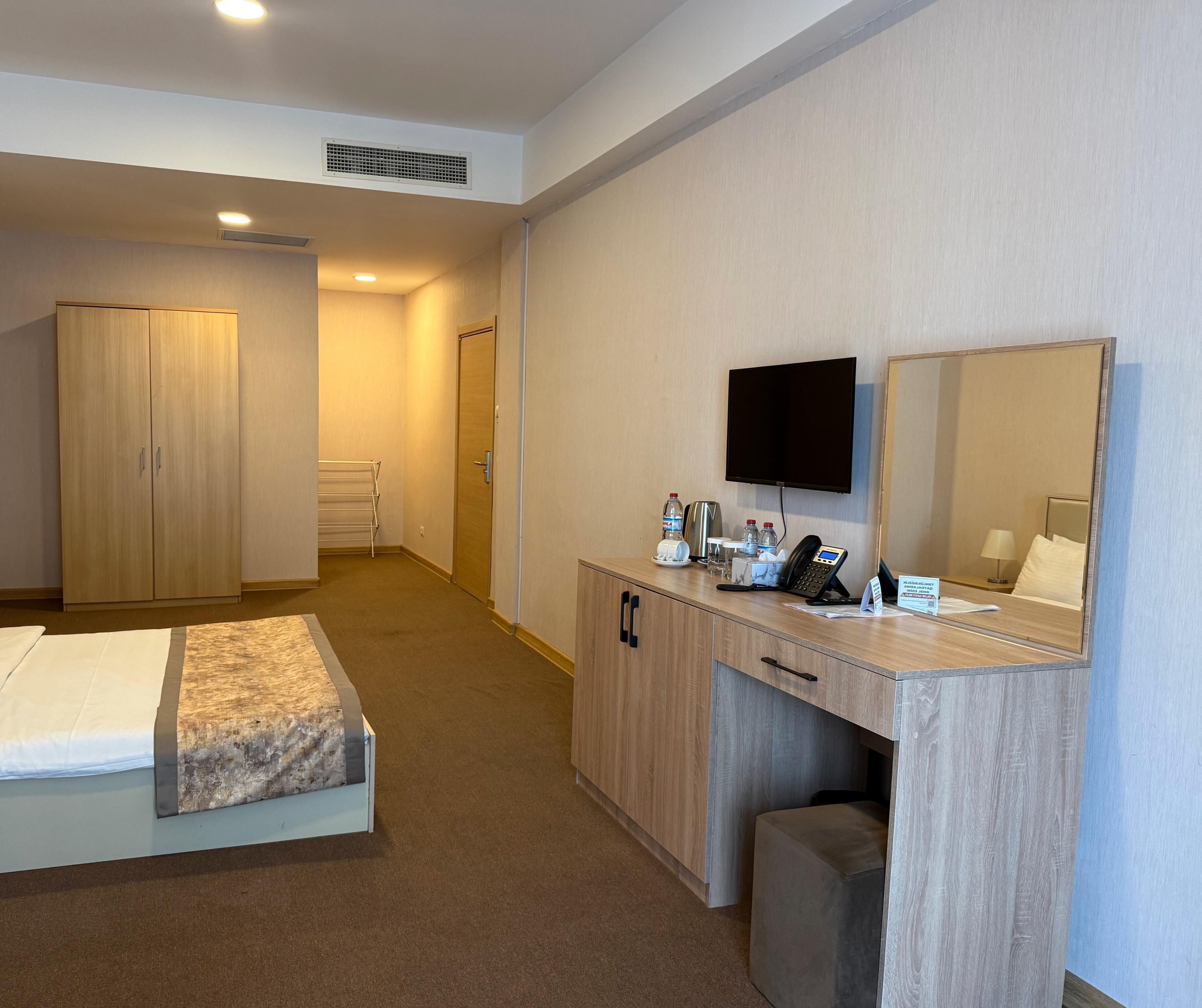 Ein Hotelzimmer mit einem Bett, einem Schreibtisch mit Telefon und Pflegeprodukten, einem Fernseher und einem Spiegel.