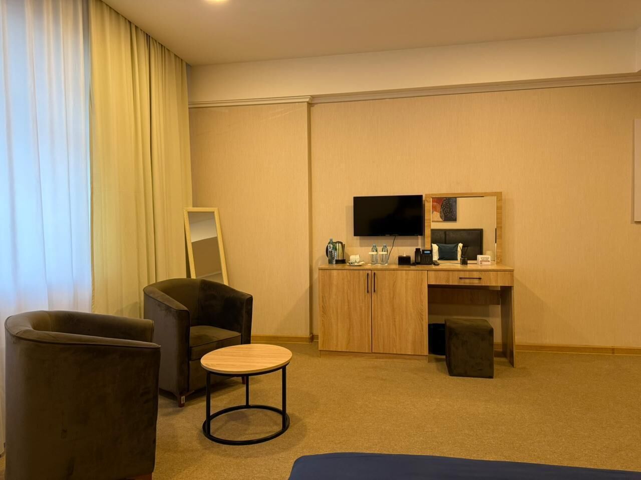 A hotel room with a seating area, a desk, a television, and a mirror.