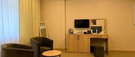 A hotel room with a seating area, a desk, a television, and a mirror.