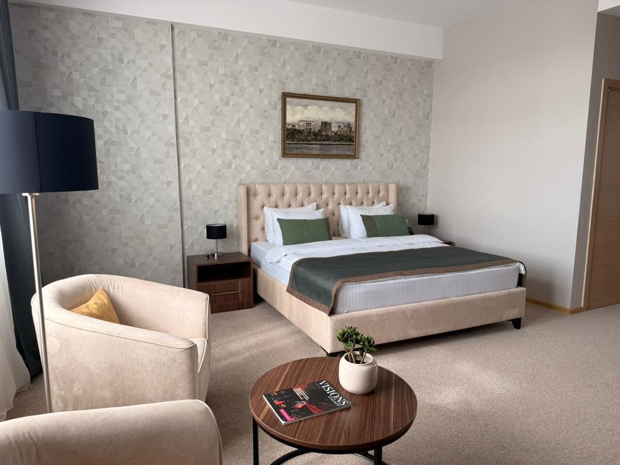 A bedroom with a bed, nightstands, a chair, a round coffee table, and a wall-mounted lamp.