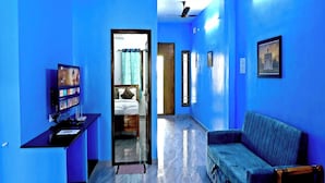 A hallway with blue walls, a bed, a desk, a sofa, and ceiling fans. - Golden Home Stay (Puducherry)