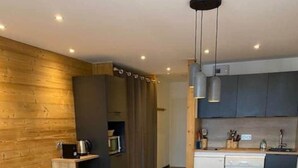 Una cocina moderna con paredes de madera, una zona de comedor con una mesa grande y sillas blancas, y una pequeña mesa redonda con una planta.