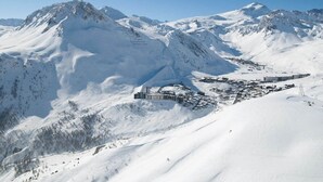 Un pueblo cubierto de nieve en la montaña, con un conjunto de edificios, incluyendo un gran hotel de varios pisos y un complejo de esquí al fondo.