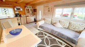 A cozy cabin interior with a dining area, kitchenette, and a sofa by a window.
