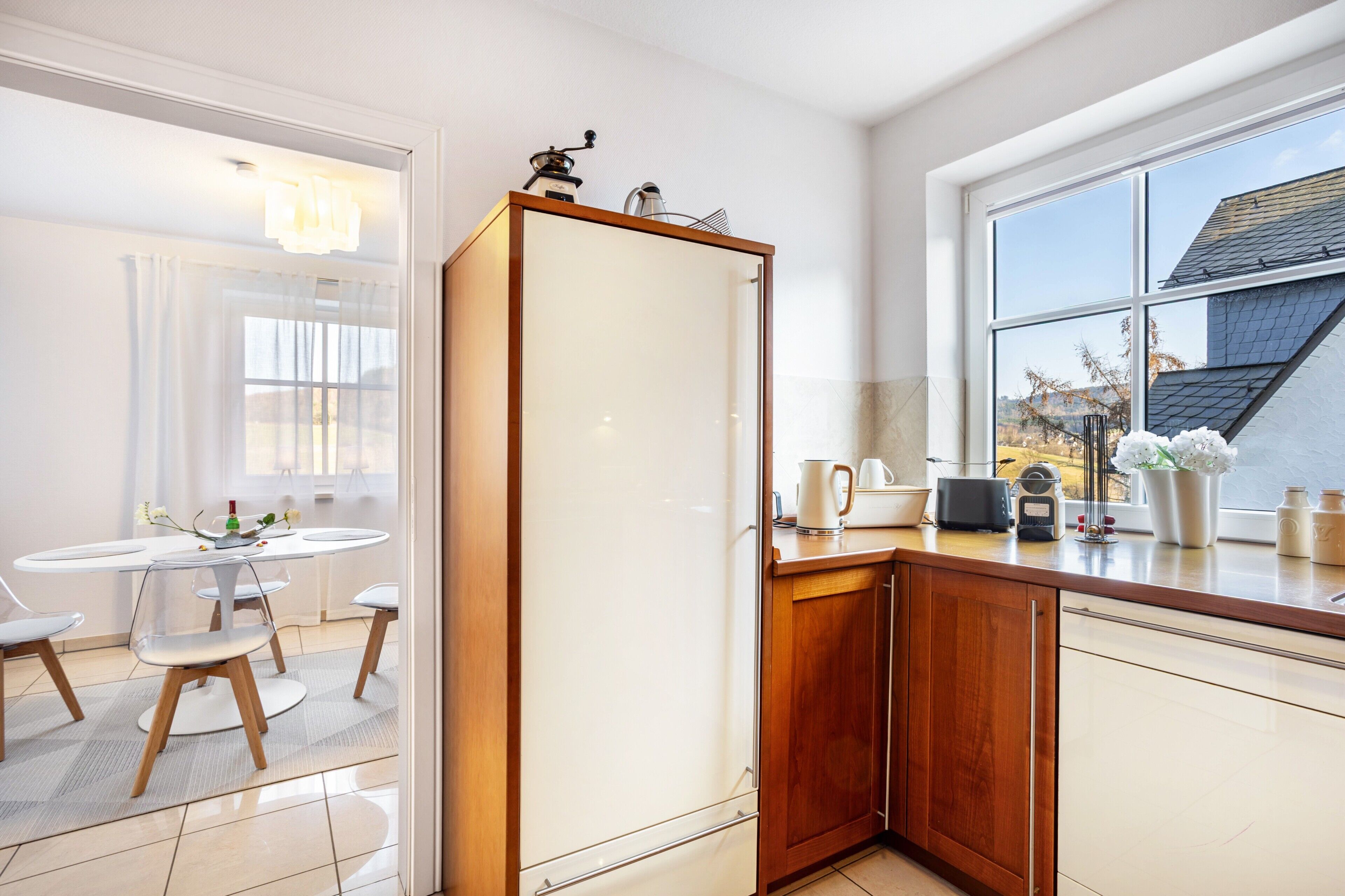 A modern kitchen with a wooden cabinet, a white refrigerator, and a window with a view of a house.