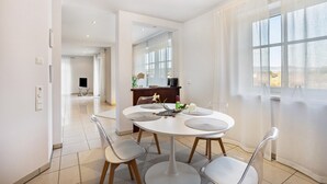 A modern dining area with a round table, four chairs, and a view of the city through large windows.