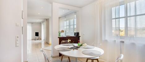 A modern dining area with a round table, four chairs, and a view of the city through large windows.