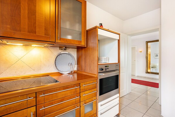 Una cocina moderna con armarios de madera, horno empotrado y una alfombra roja que conduce a un pasillo.