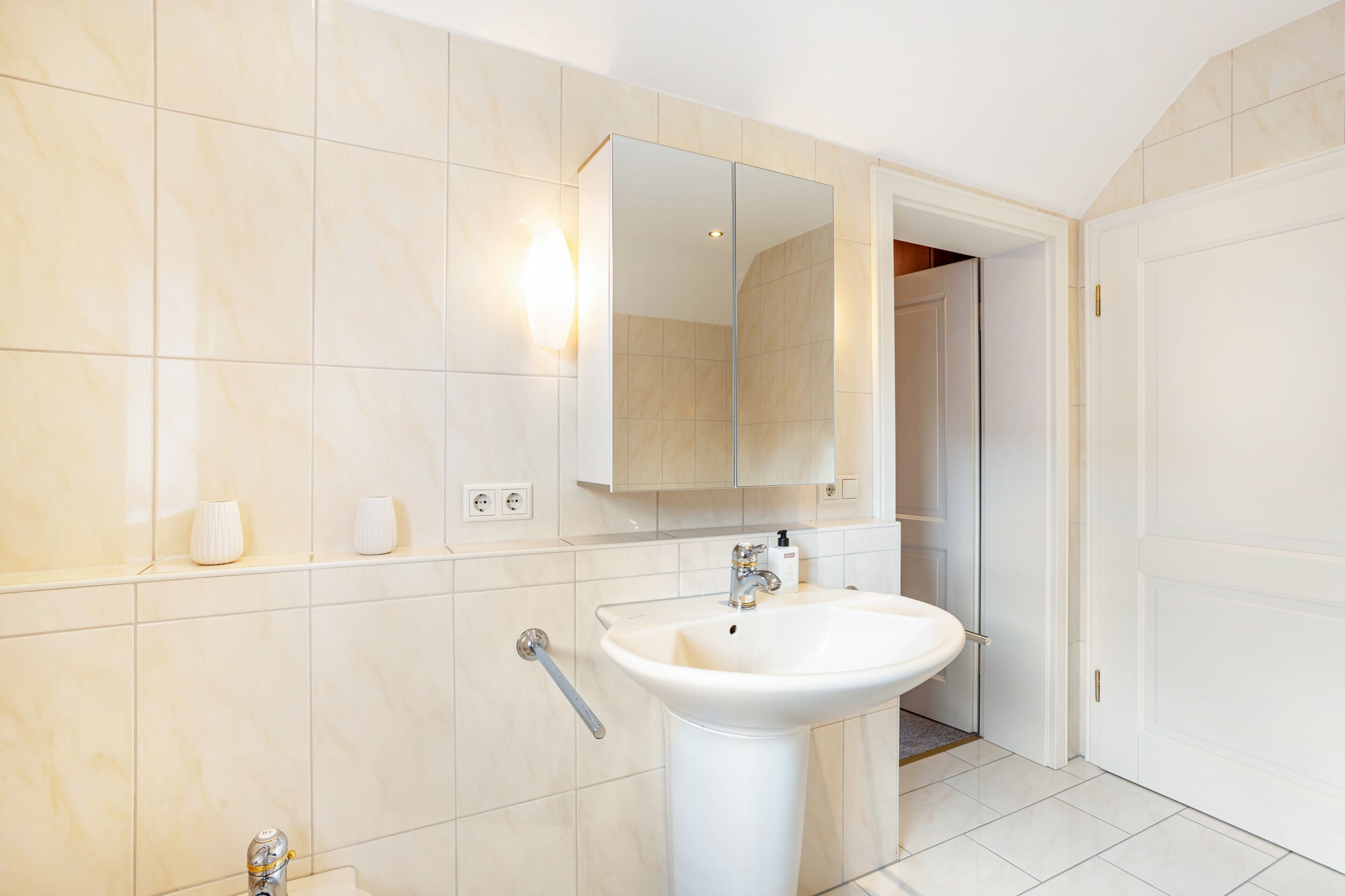 A bathroom with a white sink, a mirror, and a door leading to another room.