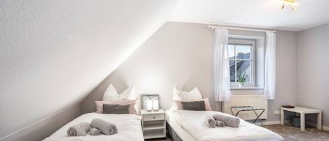 Een slaapkamer met twee bedden, een raam met gordijnen, een nachtkastje en een radiator.