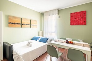 A room with a bed, a table with chairs, a window with curtains, and artwork on the walls.