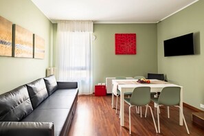 A modern living room with a sofa, dining table, chairs, a red accent wall, and a flat-screen TV.