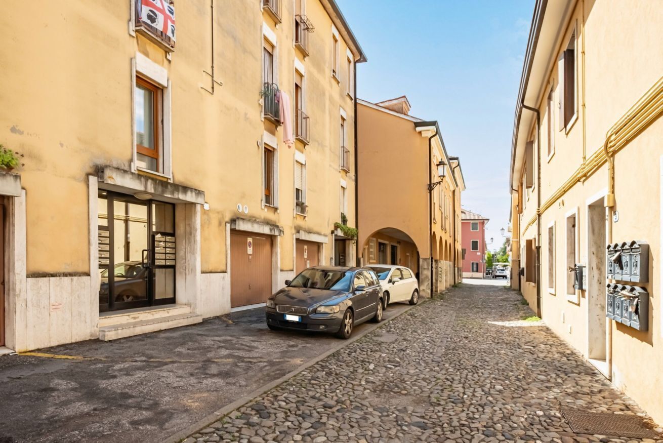 Eine enge Kopfsteinpflasterstraße, gesäumt von Gebäuden, mit einem geparkten Auto und blauem Himmel.