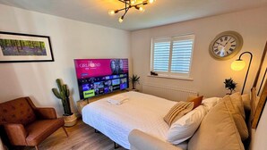 A cozy bedroom with a bed, a TV, a chair, and a small table. - Warm & Stylish Cottage in Historic Odiham (Odiham)