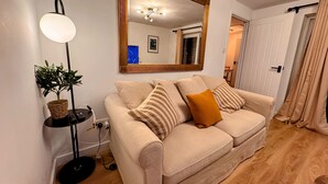 A living room with a beige sofa, a large mirror, a floor lamp, and a potted plant. - Warm & Stylish Cottage in Historic Odiham (Odiham)