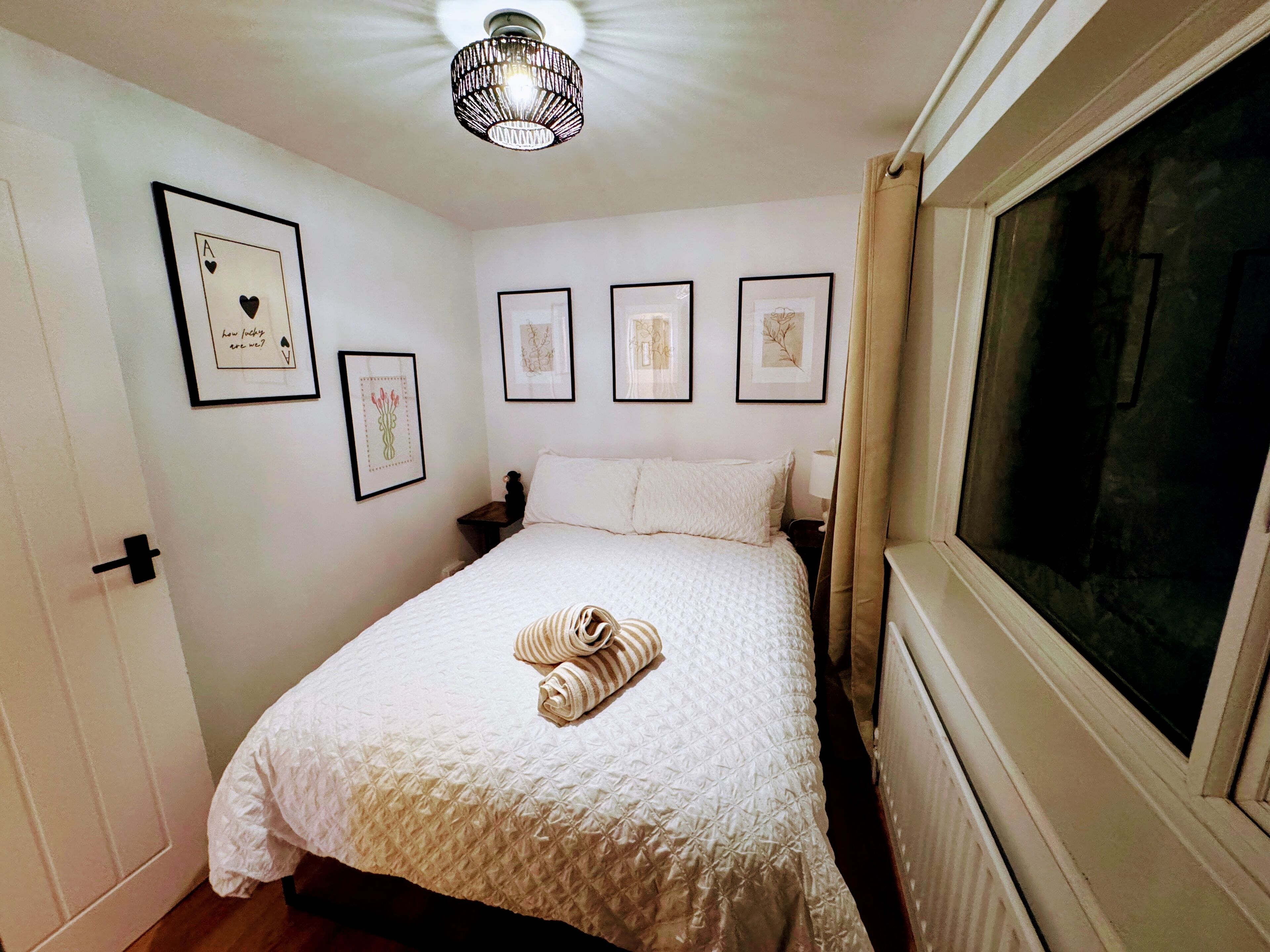 A bedroom with a bed, a window, and framed pictures on the wall.