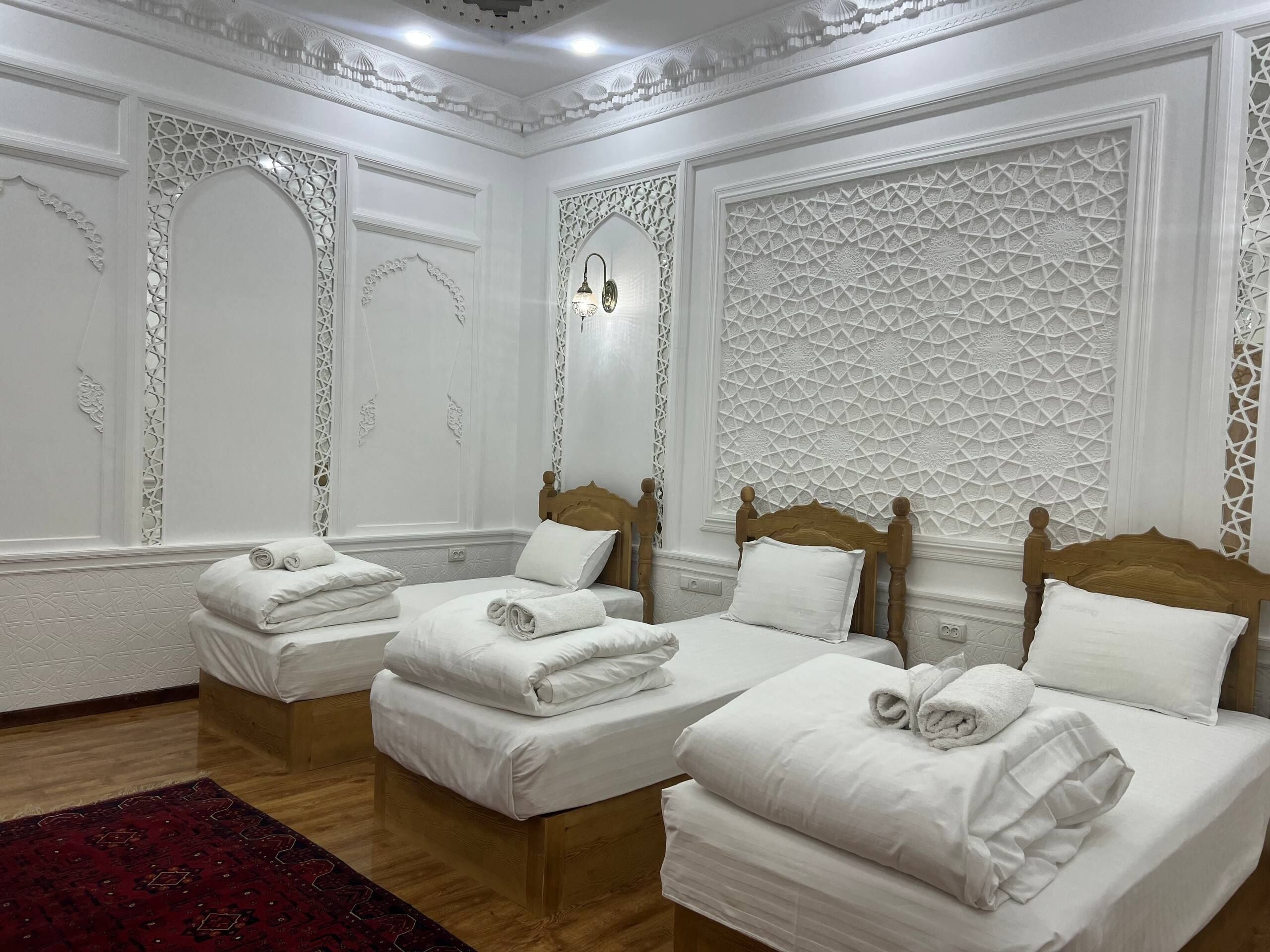 A hotel room with two beds, white linens, wooden headboards, decorative wall panels, and a red rug.