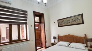 Una habitación de hotel con una cama grande, un radiador, una ventana con persianas, una puerta y un candelabro.