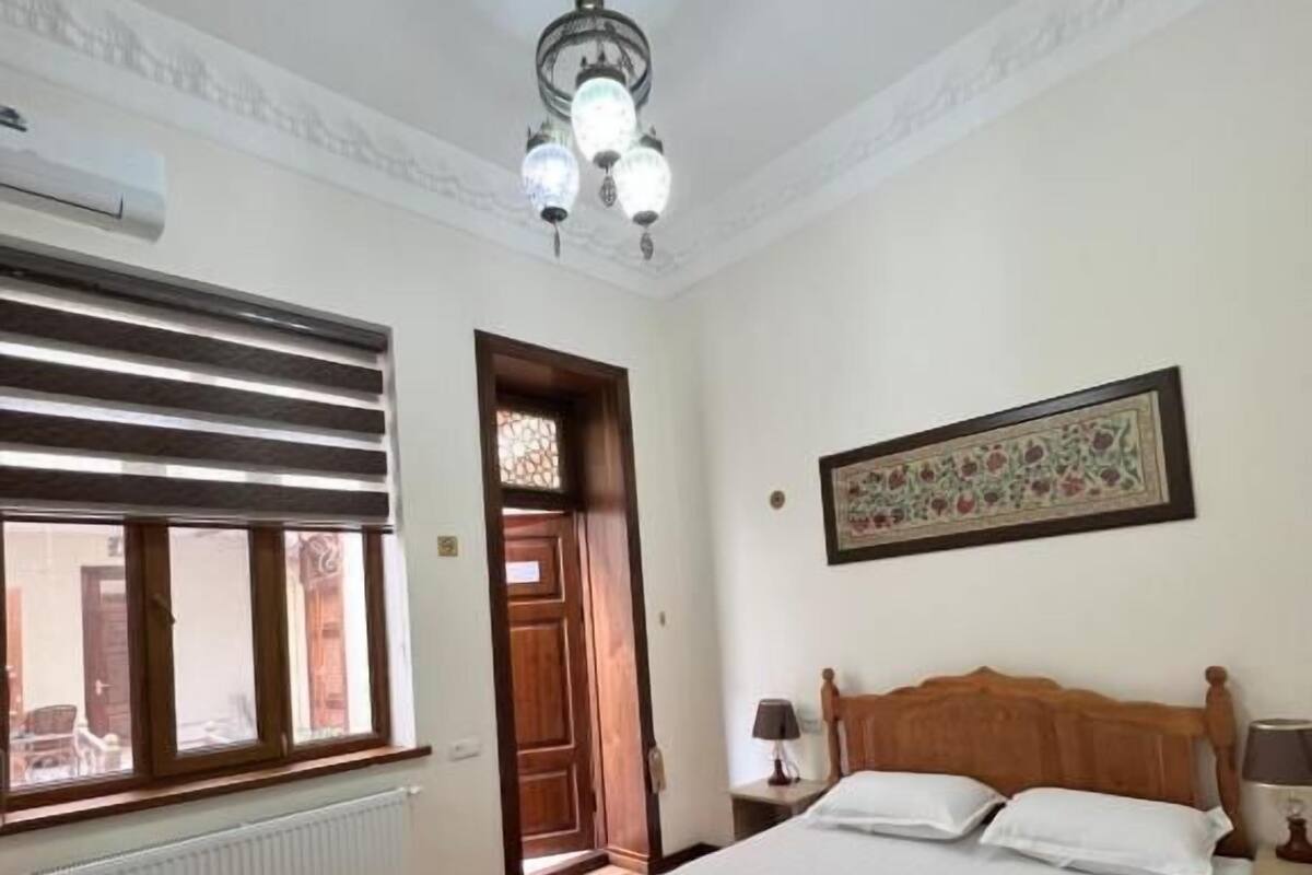 Una habitación de hotel con una cama grande, un radiador, una ventana con persianas, una puerta y un candelabro.