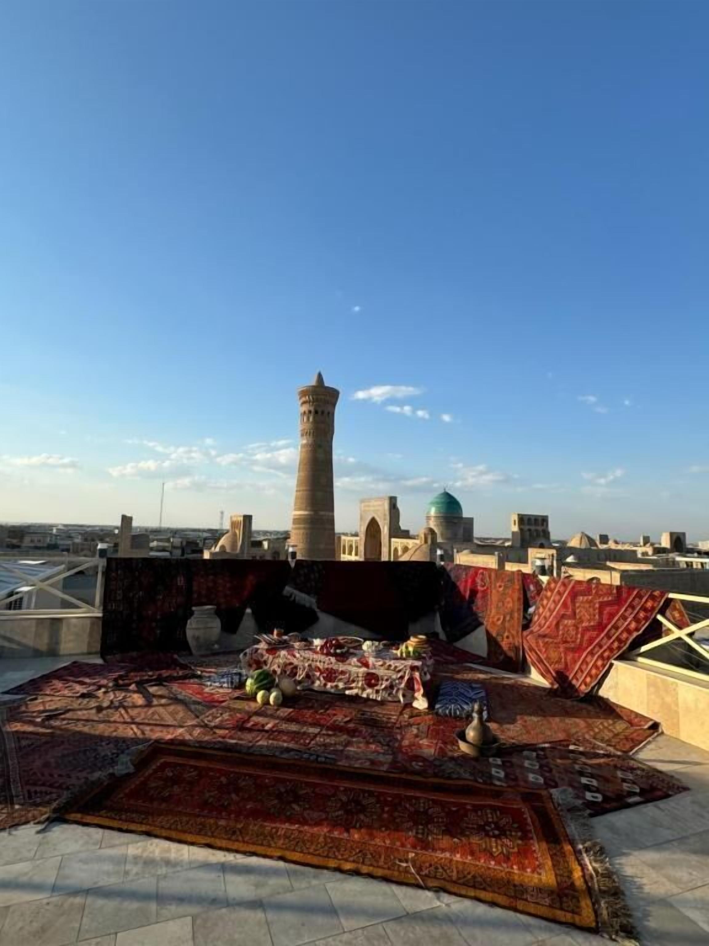 A rooftop terrace with a traditional tower, a variety of rugs, and a clear view of the cityscape.