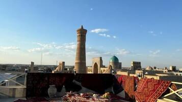 A rooftop terrace with a traditional tower, a variety of rugs, and a clear view of the cityscape.