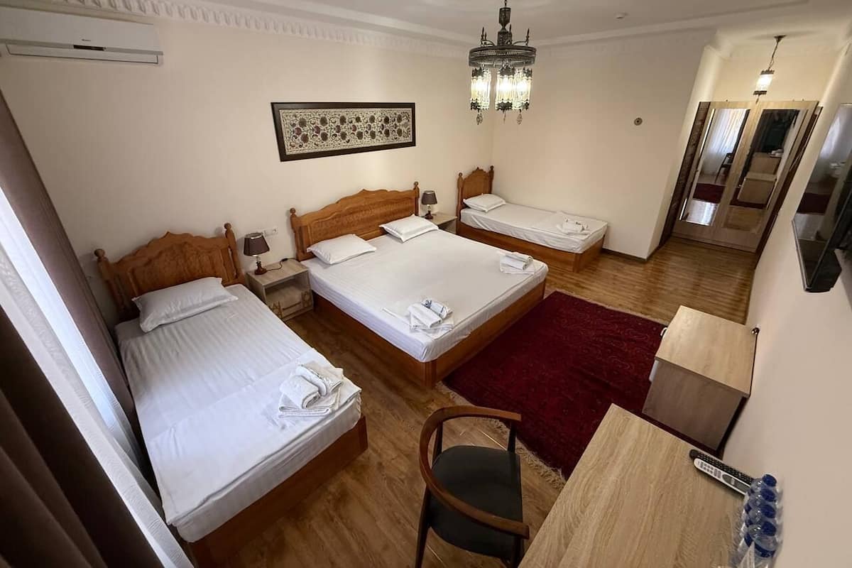 Habitación de hotel con tres camas, un escritorio de madera, una silla, una alfombra roja y un candelabro.