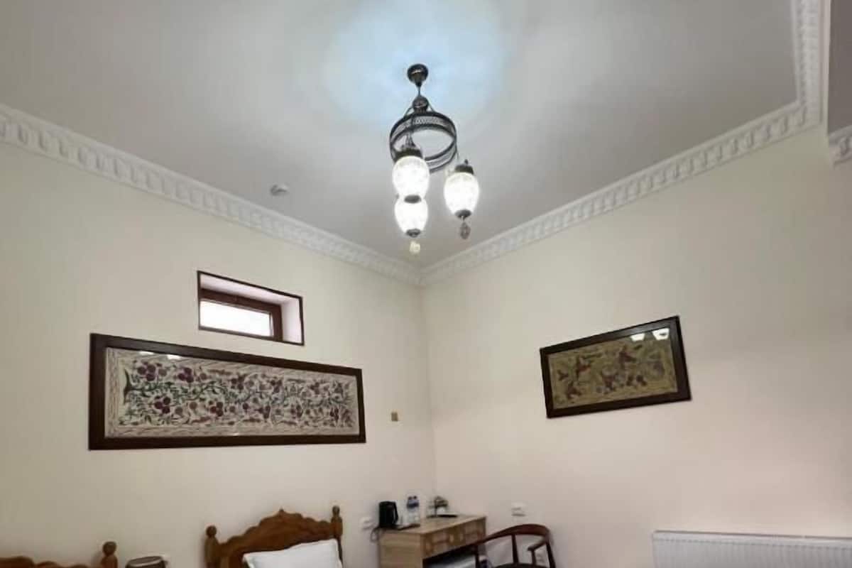 Habitación de hotel con dos camas, un escritorio, una silla, un radiador y una lámpara en el techo.